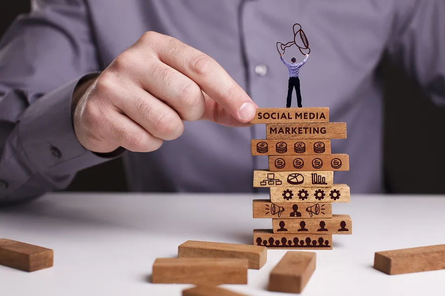 A hand stacking Jenga blocks with digital marketing terms on them