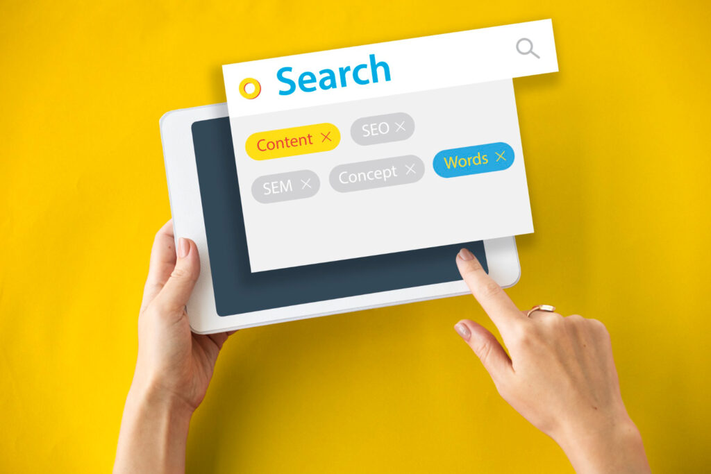 A hand holding a tablet displaying a search interface with tags such as "Content", "SEO", "SEM", "Concept", and "Words" on a bright yellow background.