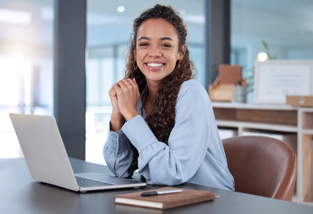 A woman smiling sitting at a laptop, with a blue shirt thinking about why seo is important. 