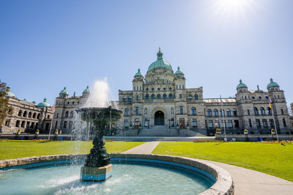 The British Columbia Parliament Buildings with a fountain in the foreground under a sunny sky in Victoria, BC, Canada, taken on April 14, 2021, showcasing the architectural grandeur and lush landscaping, ideal for tourism and educational content.
