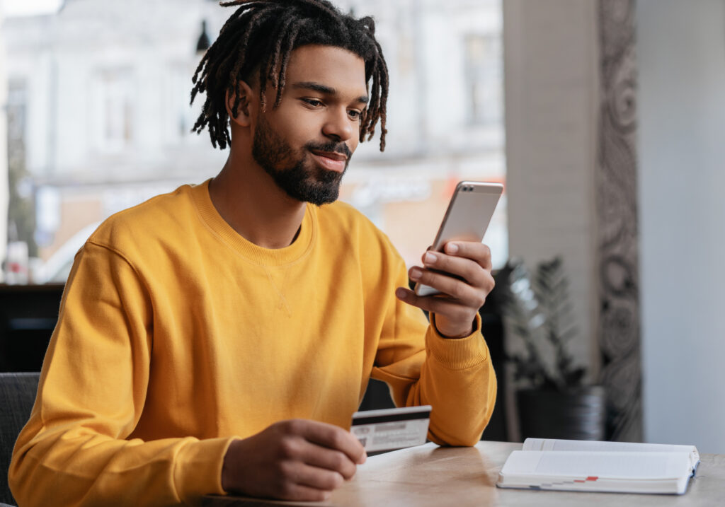 African-American man holding a credit card and smartphone possibly encountering ads from a curated Google Ads Allowed Domain List, highlighting the end-user experience of compliant digital marketing.