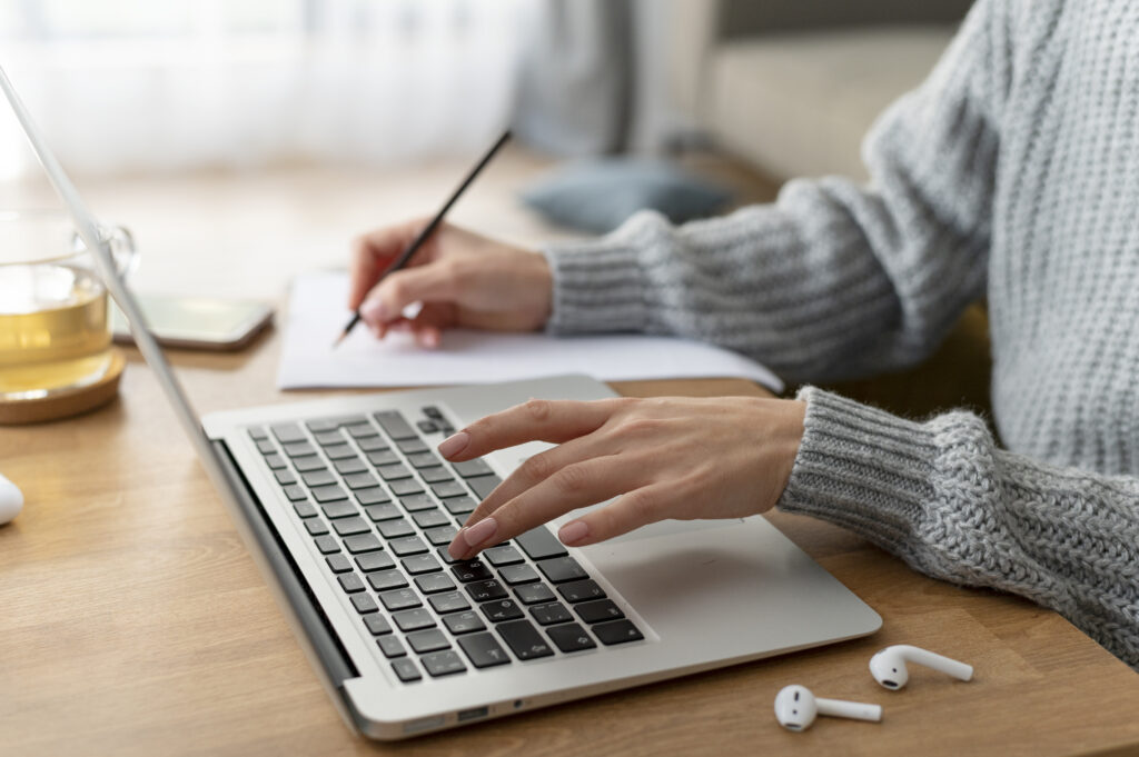 A person sits at a desk, typing and holding a pen in her hand.This image embodies the essence of creativity and productivity in the digital age, ideal for showcasing the prowess of content writing companies.