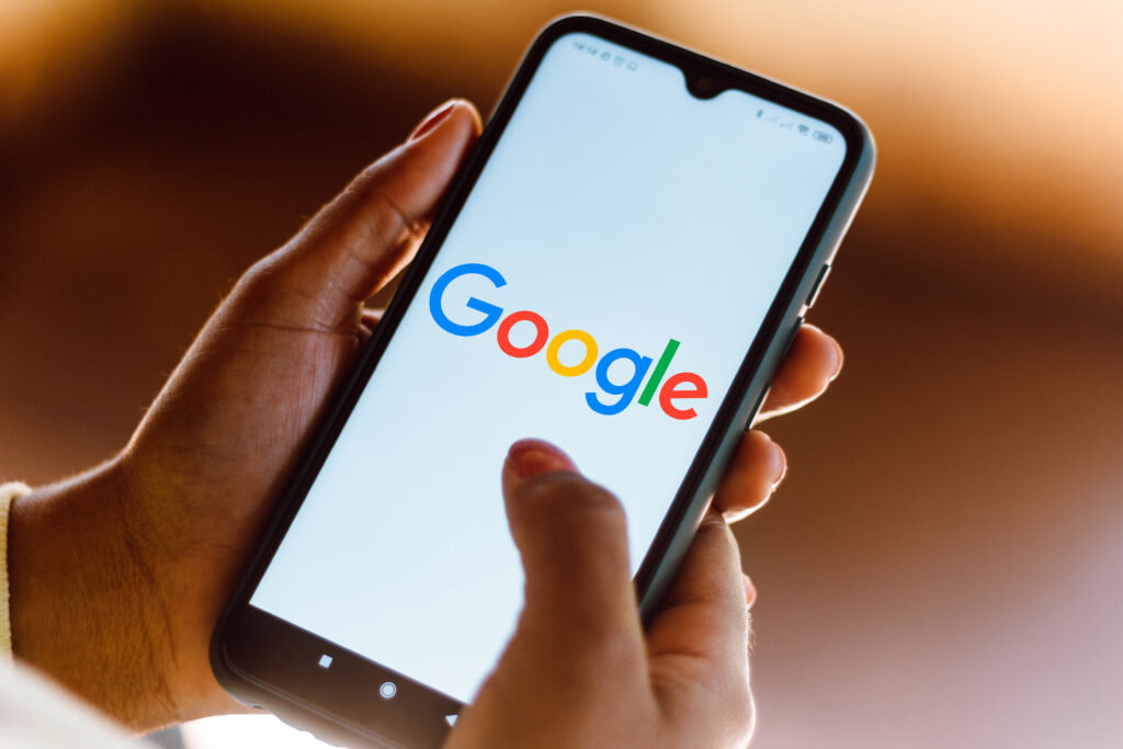 Smartphone in hand displaying the Google logo, used for services like google optimize, against a blurred background.