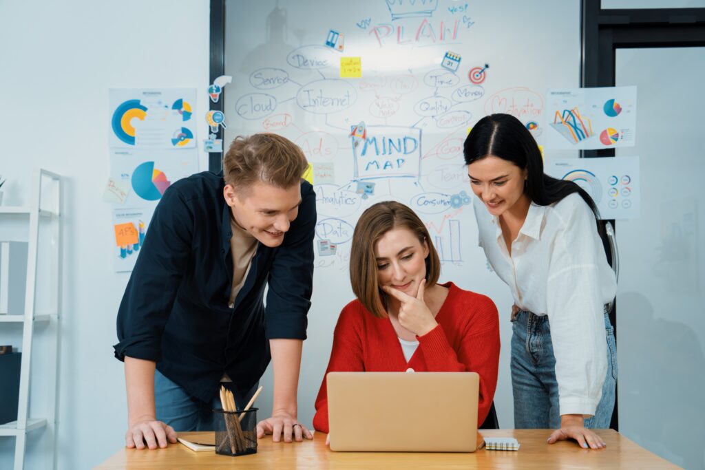 Team of three colleagues collaborating on a project with a laptop in a bright office setting, exemplifying a harmonious work environment for creating Responsive Search Ads campaigns.