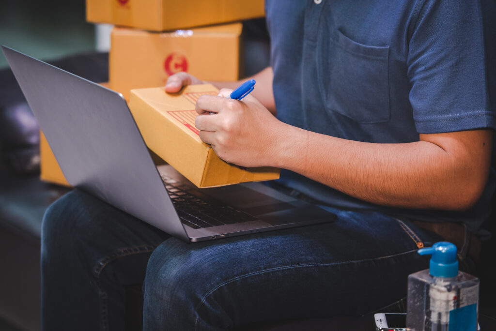 Male in a navy blue outfit signing boxes with his computer on his lap. Is Amazon FBA Canada worth it?