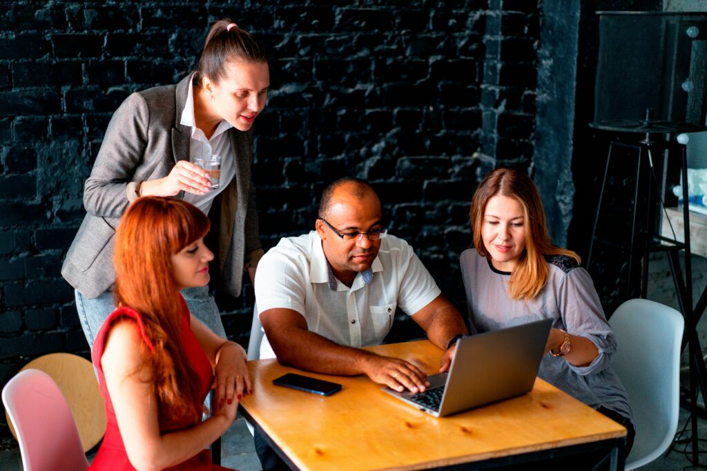 A diverse group of women and a man gathered around a laptop, discussing SEO automation tools to improve their online visibility and search engine rankings.