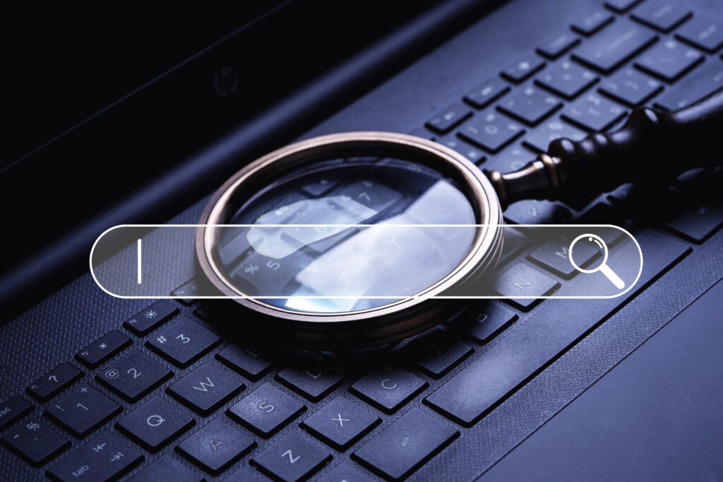 Magnifier glass on laptop computer keyboard with search bar icon for Search Engine Optimization or SEO maintenance.