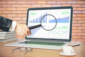 A magnifying glass held over a laptop displaying business graphs and charts, suggesting detailed analysis of data or search engine optimization performance.