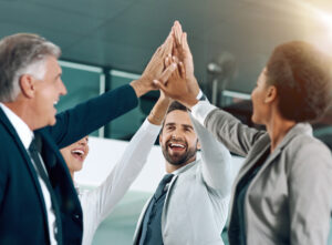 A diverse group of business professionals high-fiving in celebration, illustrating how teamwork and collaboration define strategic marketing success through shared efforts in achieving common objectives.