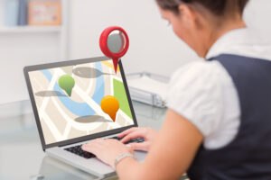 A professional workspace with a woman using a laptop to analyze a digital map with colorful location markers, emphasizing local search services.