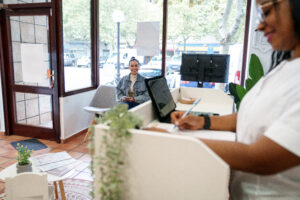 A receptionist filling out forms at a front desk while a patient waits in a bright and welcoming office, illustrating the importance of local search optimization services for attracting and managing customers effectively.