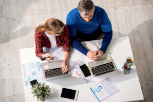 Two professionals collaborating on laptops at a desk, analyzing charts and graphs. Perfectly illustrating teamwork and "online digital marketing services."