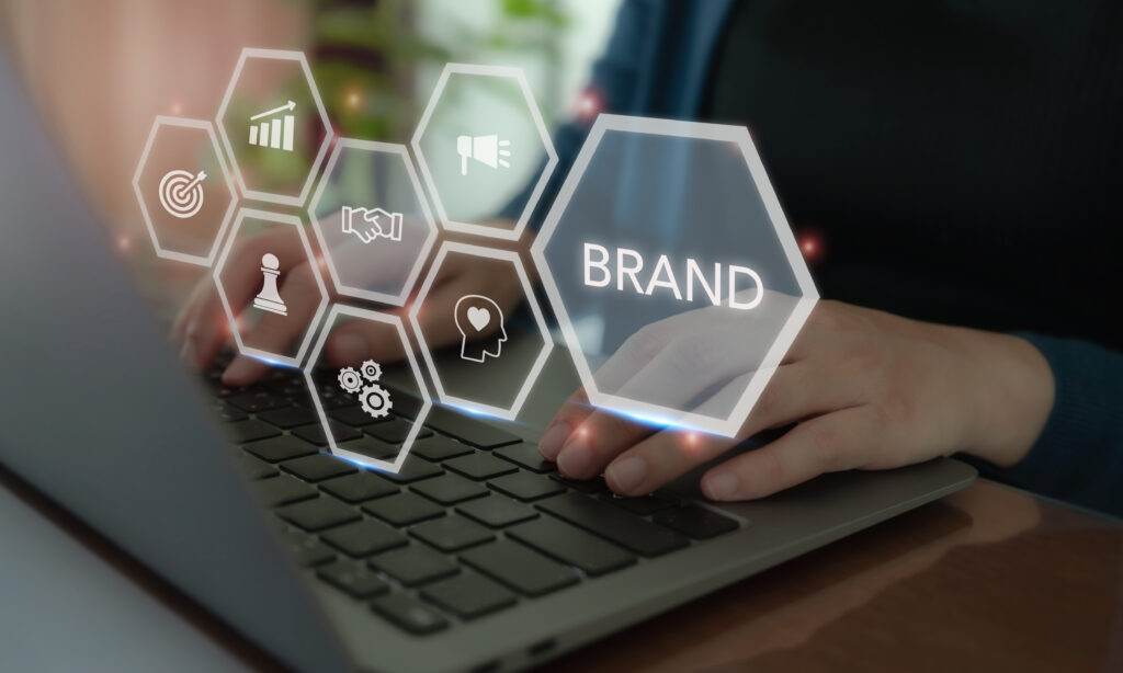 Business and branding concept. Creating, developing and maintaining a brand's identity and market reputation. Strategic planning, positioning and communication to establish a strong brand image. A futuristic visualization illustrating what is brand development strategy, featuring interconnected hexagonal icons like a target, chess piece, and megaphone overlaying hands typing on a laptop keyboard.