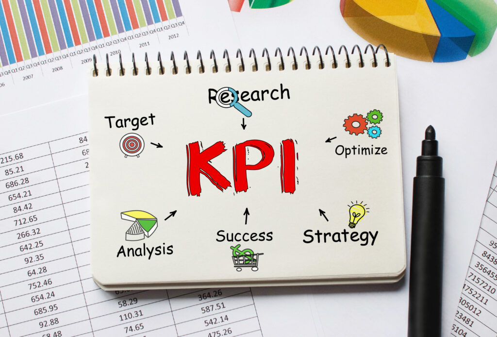 Notebook with the word 'KPI' in red at the center, surrounded by icons and words including Target, Research, Optimize, Strategy, Success, and Analysis, representing key performance indicator concepts.