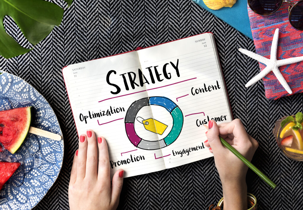 Promotion Product Strategy Marketing Concept A person is sketching a colorful marketing strategy diagram in a notebook, featuring elements like content, customer, engagement, promotion, and optimization. Surrounded by summer-themed items like watermelon slices, sunglasses, and a drink, the image visually represents marketing tips for small business in a creative and relaxed setting.