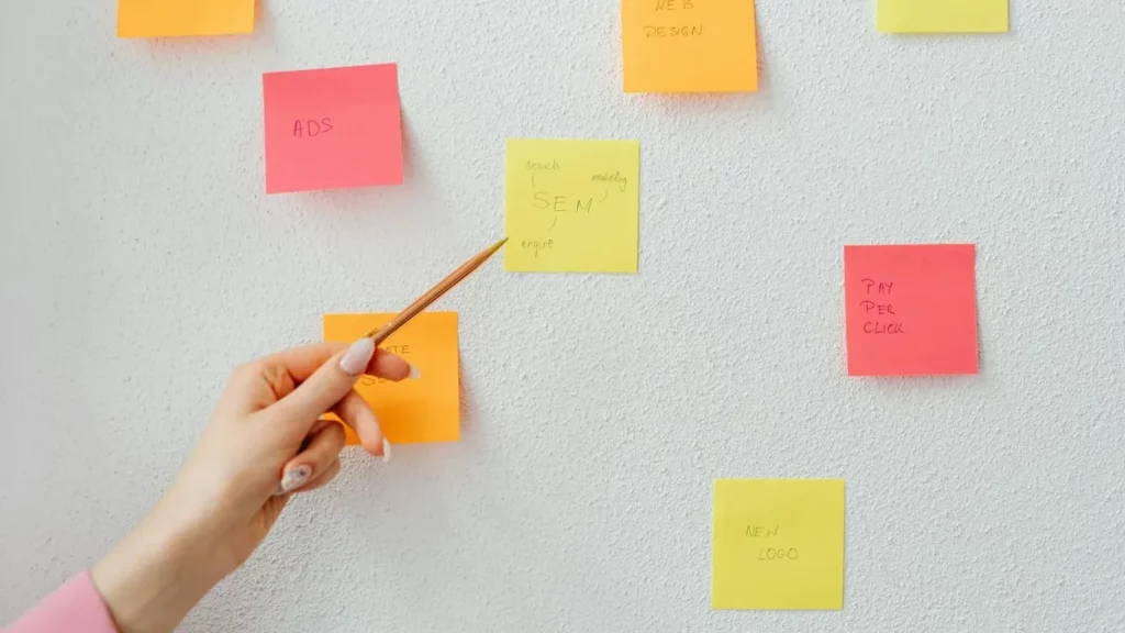 A person pointing at a yellow sticky note on a whiteboard filled with colorful notes, symbolizing planning and strategy development for Google Ads remarketing strategies.