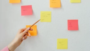 A person pointing at a yellow sticky note on a whiteboard filled with colorful notes, symbolizing planning and strategy development for Google Ads remarketing strategies.