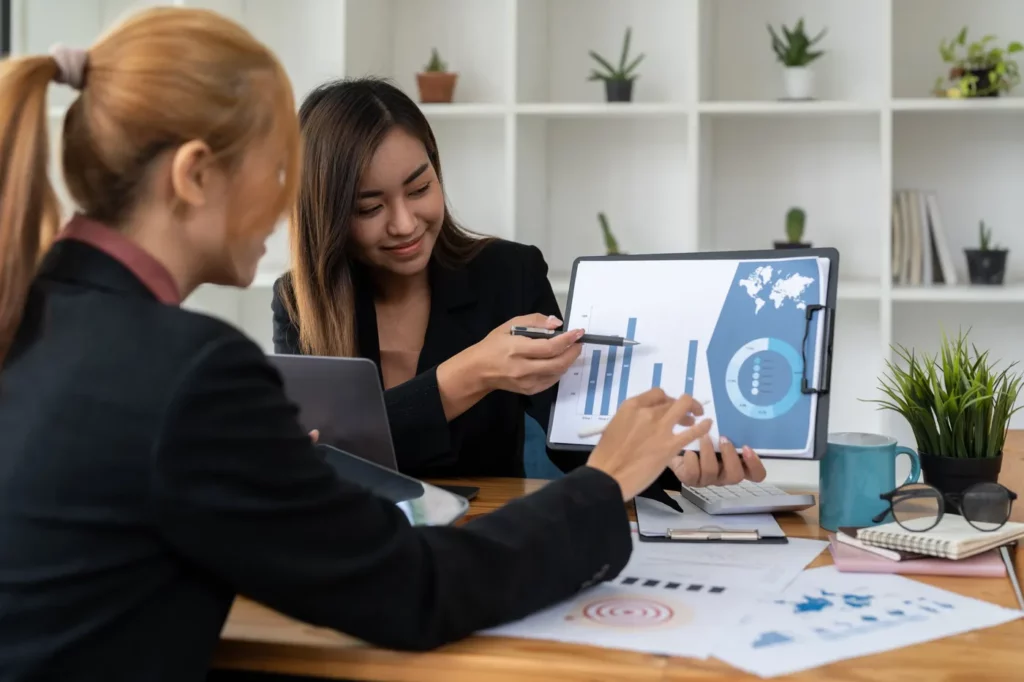 Google ads account structure being analyzed by two business women reviewing data on a clip board in a minimalist clean and bright office with many plants 