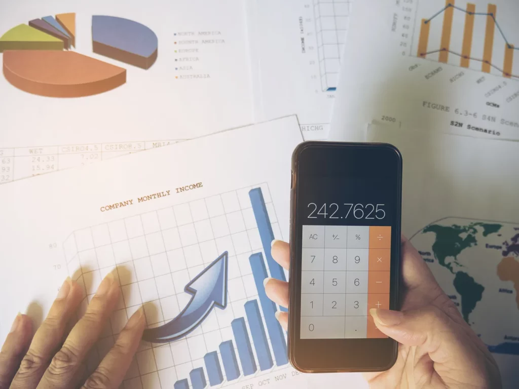 Google ads campaign budget constraints being mitigated by a business woman holding a smart phone with the calcutaor open while reviewing data charts 