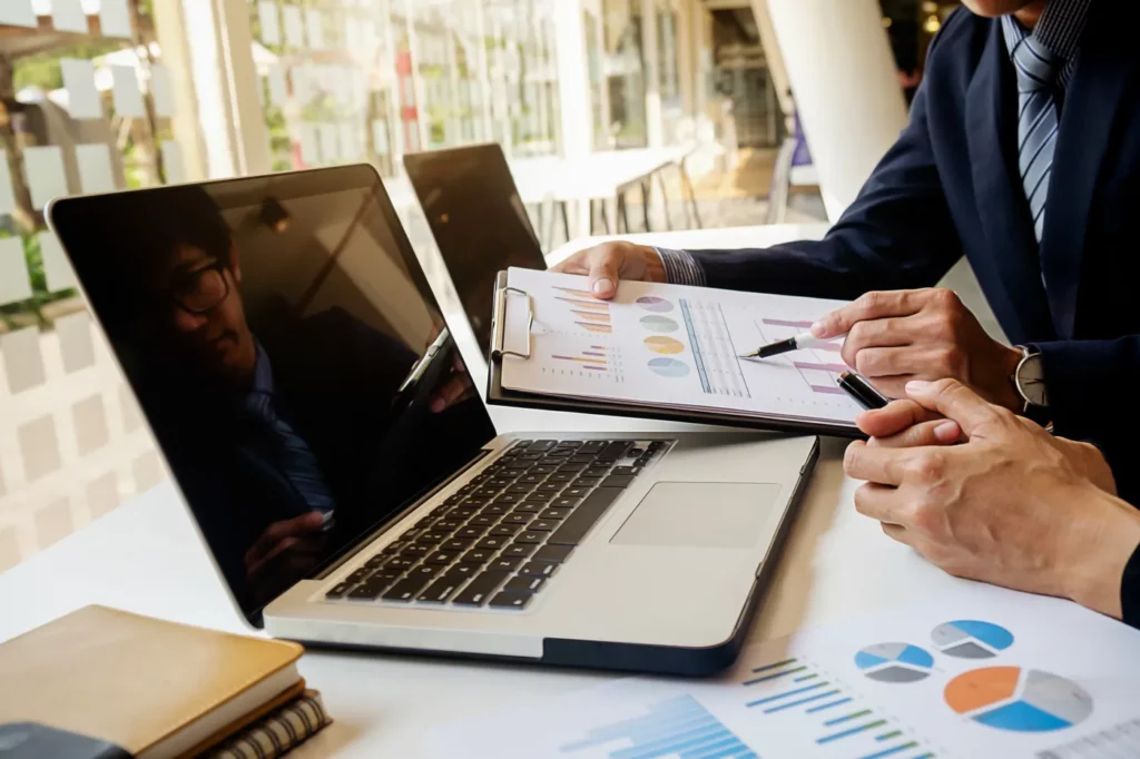 person-report-consulting-account-people-table Google ads performance planner insights being alayzed by office professional holding clip board in front of laptop