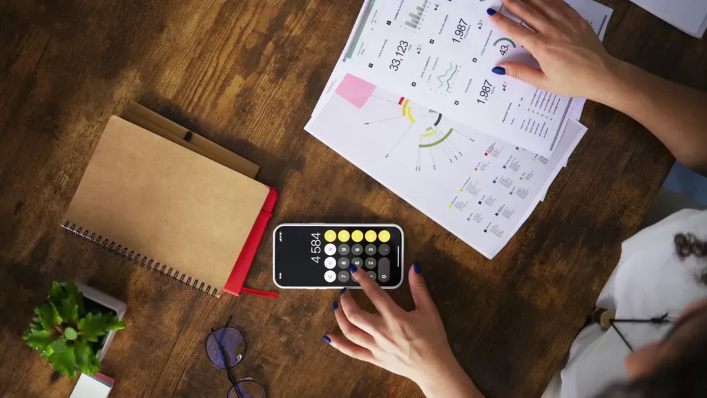 Google ads conversion optimizer being implemented by a business professional sitting at a desk with paperwork showing charts and budget while she uses a calculator to work out the budget 